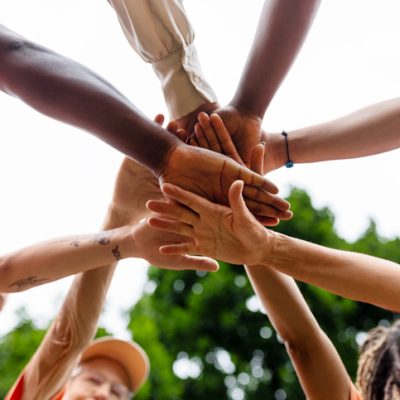 Directly below shot of multiracial volunteers stacking hands during environmental cleanup program. Multiethnic men and women cheering before cleaning the city park.